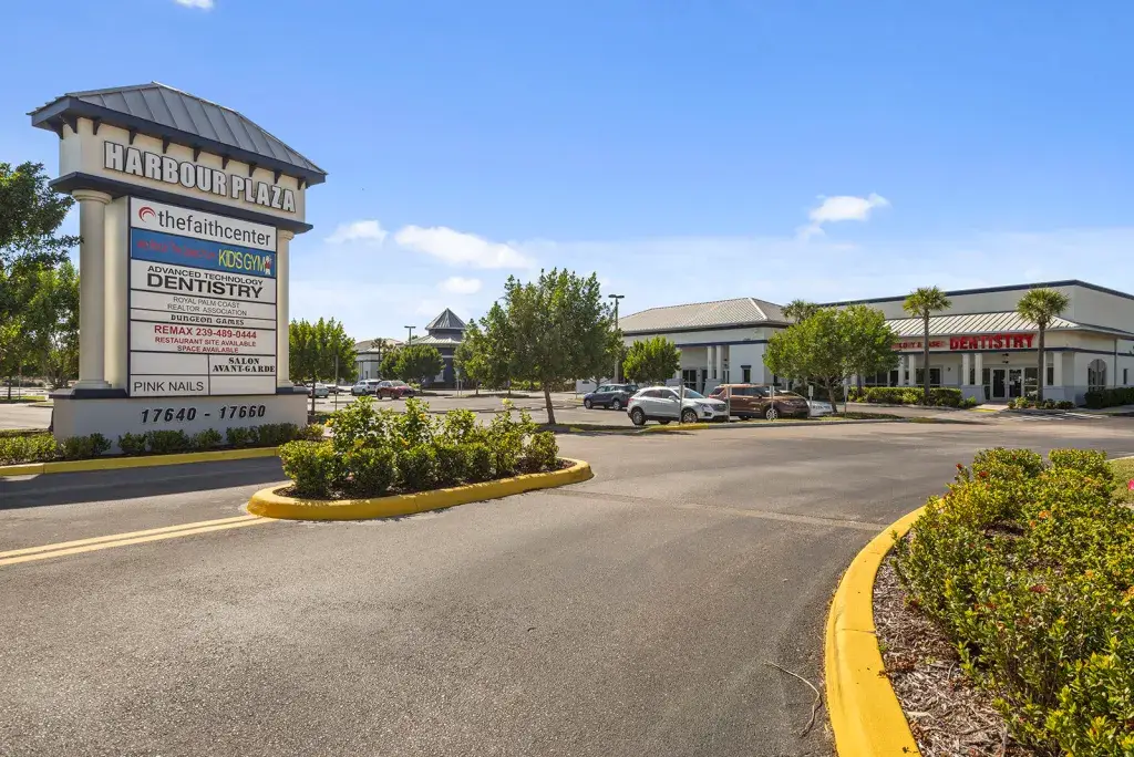 Front view of Harbour Plaza in Fort Myers, Florida, featuring the property's marquee sign, shopping center storefronts, landscaped entrance, and customer parking area.